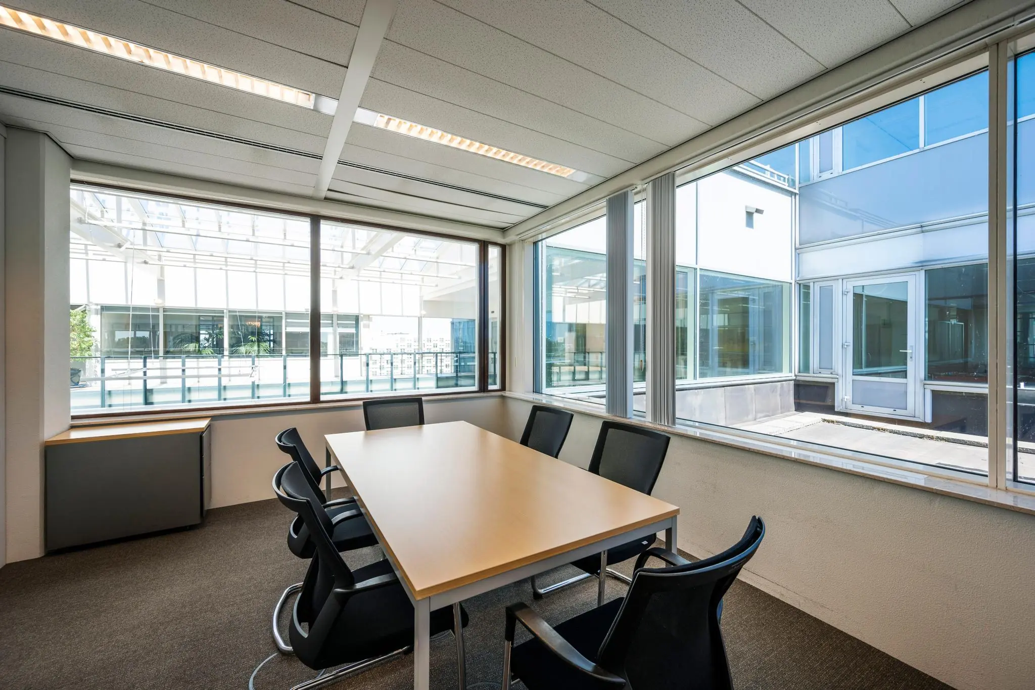 Vergaderruimte met zes stoelen en grote ramen in een modern kantoorpand aan de Thomas R. Malthusstraat.